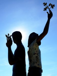 A silhouetted view of the sculpture at the front of the YOC campus, depicting a boy and a girl with branches growing from their raised hands.